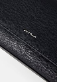 Portafoglio in pelle nera con texture e finitura liscia, con il logo "Calvin Klein" in argento. Design semplice caratterizzato da linee pulite e senza ulteriori abbellimenti.