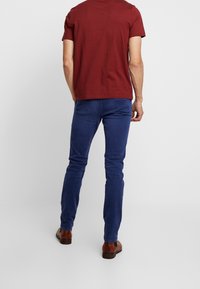 Mörkröd bomulls-t-shirt tillsammans med blå slim fit-byxor och bruna skor. T-shirten har en rund hals; byxorna har en jämn textur.