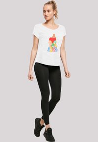 White short-sleeve t-shirt with colorful cartoon characters and a red heart graphic, paired with black leggings and black sneakers.