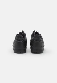 Svarta sneakers med ovandel i slätt läder, vadderad krage och texturerade detaljer; har logotypdetaljer på hälen och tungan.