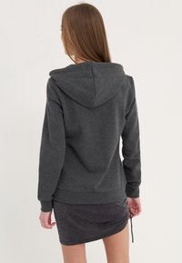 Sudadera con capucha de color gris oscuro y corte relajado, con puños y dobladillo de canalé, combinada con una falda corta negra brillosa.
