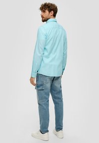 Himmelblaues Langarmhemd mit Button-Down-Kragen, kombiniert mit hellblauen Cargo-Jeans und weißen Sneakern; sichtbare Nähte und Taschen.