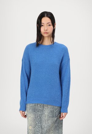 Blauwe trui van donzig materiaal met een ronde hals en geribde boorden, gecombineerd met een gestructureerde slangenhuid rok.