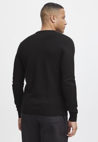 Black knitted sweater featuring a textured pattern, ribbed cuffs, and hem. It has a classic crew neckline and a relaxed fit in the back view.