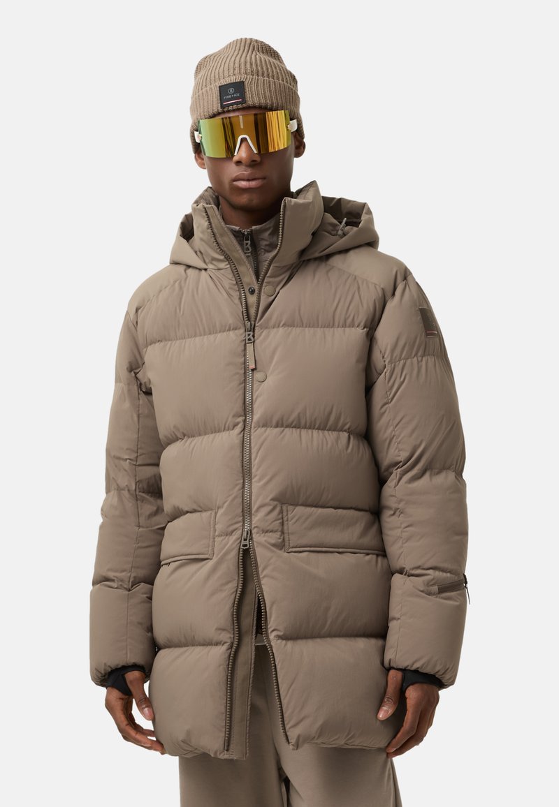 Beige puffer jacket with a zip front, hood, and two front pockets. Includes a ribbed knit beanie and reflective yellow sunglasses.