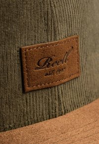 Green corduroy hat with a brown leather patch labeled "Beell" and stitching details. The brim is wide and made of a textured material.