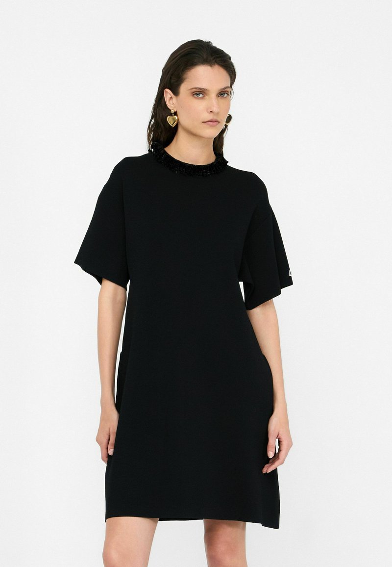 Schwarzes kurzes Kleid mit lockerer Passform, das einen Rüschenkragen, weite Ärmel und Seitentaschen hat. Glattes Material mit moderner Silhouette.