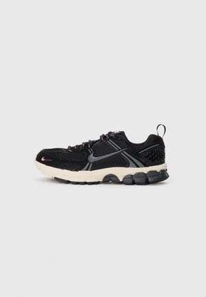 Baskets de course Nike noires et grises avec un dessus en maille, semelle blanche rembourrée, lacets multicolores et languette au talon sur fond blanc.