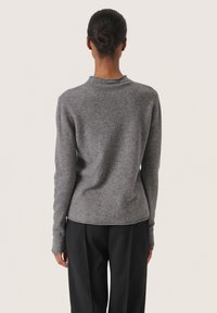 Grauer gestrickter Pullover mit hohem Kragen, langen Ärmeln und strukturiertem Oberflächenmuster, kombiniert mit schwarzen Hosen, von hinten betrachtet.