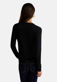 Zwarte trui met lange mouwen, textuurstof en geribbelde manchetten, gecombineerd met donkerblauwe jeans met contrasterende oranje stiksels.