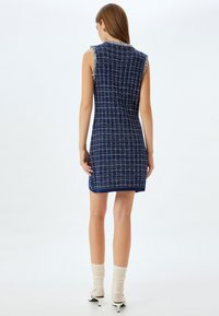 Laivansiniset hihattomat mekko, strukturoidusta tweed-kankaasta, jossa on ruutukuvio. Ominaisuuksina on fringetyksillä varustettu kaulus ja tiukka siluetti.