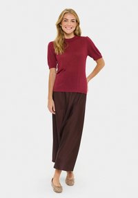 Burgundy short-sleeve knit top with ribbed neckline, paired with wide brown trousers and embellished light-colored flats. Smooth texture overall.