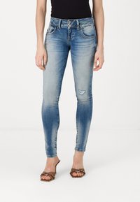 Smal jeans i ljusblå denim med blekningar, fem fickor och en sliten detalj på vänster ben. Bärs med bruna klacksandaler.