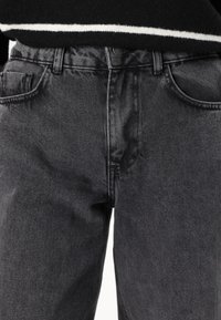 Jeans de mezclilla negra con un acabado deslavado, diseño de cinco bolsillos, costuras visibles y cierre de botón en la cintura.