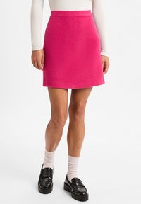 Fuchsia A-Linienrock aus strukturiertem Stoff, mit hoher Taille und geradem Saum. Kombiniert mit schwarzen Slippern und hellen Socken.