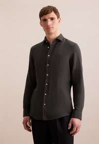 Camicia verde scuro a maniche lunghe realizzata in tessuto strutturato con colletto button-down, caratterizzata da bottoni bianchi lungo la parte anteriore e orlo curvo.