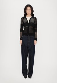 Black lightweight knit cardigan with open mesh design, button front, paired with high-waisted dark denim pants, and pointed toe black shoes.