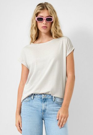 Junge Frau mit rosa rechteckigen Sonnenbrillen, einem weiß-beigen gestreiften Kurzarmtop und hellblauen Jeans, die vor einem schlichten Hintergrund posiert.