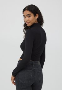 Maglia nera a collo alto a coste con maniche lunghe, design cropped. Abbinata a jeans grigi scuri a vita alta con tasche posteriori.