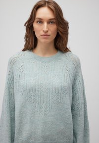 Hellblaues Strickpullover mit einem strukturierten Zickzackmuster, rundem Ausschnitt und lockerer Passform. Hergestellt aus weichem, luftigem Material.