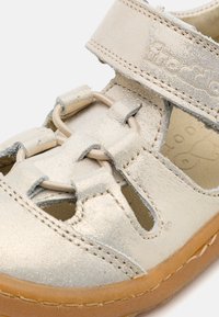 Sølv lær sandaler med utskjæringsdesign, elastisk snøring og borrelåsreim. Har en slitesterk tan gummisåle. Teksturet metallisk finish.