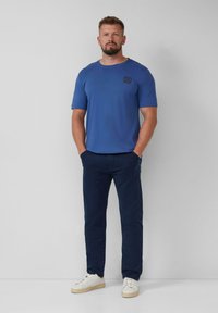 Blauwe t-shirt met korte mouwen en een borstlogo, gecombineerd met marineblauwe broek en witte sneakers. Effen kleuren, klassieke pasvorm, zachte stof.