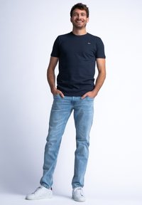 Marineblauw katoenen t-shirt met korte mouwen, gecombineerd met lichtblauwe jeans en witte sneakers. Eenvoudig ontwerp, geen prominente patronen of accenten.