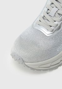 Scarpa da ginnastica grigio chiaro con tomaia in tessuto a rete strutturato, lacci piatti e suola a strati con piccoli tacchetti antiscivolo sul fondo.