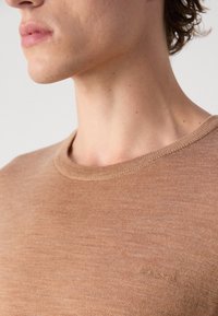 Brown cotton sweater with a ribbed round neckline and subtle texture. Features a small logo stitched in the bottom corner.