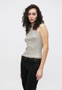 Paski, prążkowany top na ramiączkach w kremowym i czarnym kolorze, z wysokim dekoltem i dopasowanym krojem. Noszony z czarnymi dżinsami i paskiem z ćwiekami.