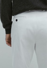 Bia�łe spodnie o gładkiej fakturze, z tylną kieszenią zapinaną na czarny guzik. Materiał wydaje się lekki i dopasowany.
