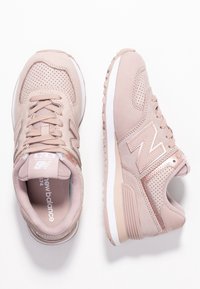 Vaaleanpunaiset New Balance 574 -lenkkarit, joissa on mokka- ja verkko-osa, rei'itettyjä yksityiskohtia, nauhat ja valkoinen kumipohja. Metallinen logokuvio.