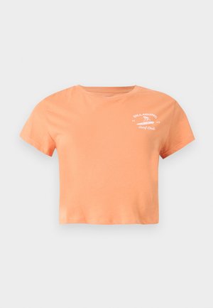 T-shirt court de couleur pêche avec manches courtes, col rond et logo blanc "Billabong Surf Club" sur le haut gauche de la poitrine.