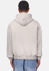Sweatshirt à capuche gris clair avec une coupe décontractée, des poignets et un ourlet inférieur côtelés. Fabriqué en tissu doux avec une texture lisse.