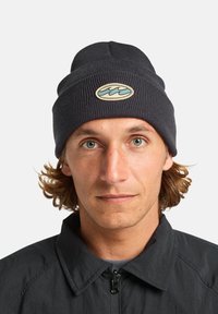 Gorro de punto de color gris oscuro que presenta un patrón texturizado y un parche circular en la parte delantera con un diseño de ola azul.