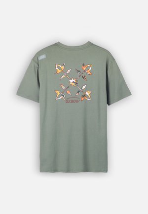 T-shirt en coton vert avec un motif floral en orange, blanc et noir au dos, avec une petite étiquette de marque sur l'épaule gauche.