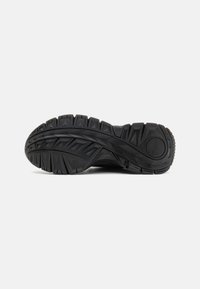 Semelle de chaussure en caoutchouc noir avec un design texturé comprenant des profondes rainures et un logo circulaire. Durable et conçue pour une traction sur diverses surfaces.