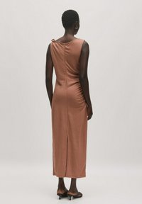 Maxikleid aus weichem, rostfarbenem Stoff. Verfügt über einen runden Ausschnitt, seitliche Raffung und einen Schlitz hinten für Bewegungsfreiheit.