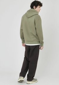 Sweat à capuche vert olive avec une coupe décontractée et un cordon de serrage, associé à un pantalon marron foncé et des baskets à motifs.