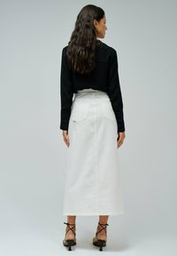 Jupe maxi en denim blanc avec deux poches arrière, taille haute et coutures contrastantes, associée à un haut noir à manches longues et des talons à lanières.