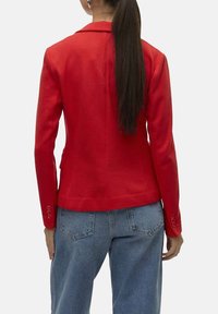 Blazer rouge au design structuré, à manches longues, col à revers et subtils accents de boutons. Associe avec un jean en denim bleu clair.