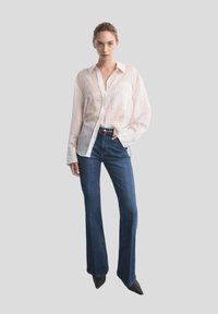 Camicia a maniche lunghe a righe leggere, con bottoni, in rosa pallido e bianco, abbinata a jeans svasati di un blu scuro e tacchi a punta neri.