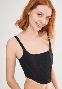 Bralette in pizzo nero con scollatura quadrata, spalline sottili e silhouette aderente. Motivo floreale testurizzato con bordi lisci e costruzione curata.