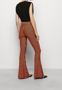 Svart ärmlös topp med orange och svarta randiga utsvängda byxor, som har vertikala ränder och en figurnära midjedesign.