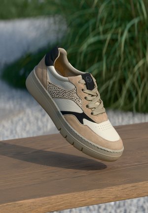 Beige och vit sneaker med material av mocka och läder, rundad form, perforerade accenter och detaljer i svart på hälen. Gummisula.
