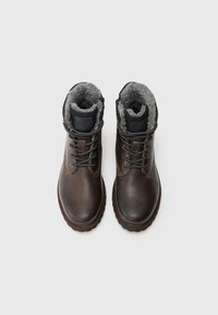 Botas de cuero marrón con superficie texturizada, forro de piel, ojales de metal y suela de goma. Diseño con cordones y logo en la lengüeta.