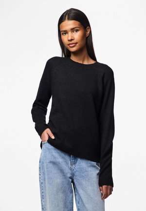 Schwarzer Strickpullover mit rundem Ausschnitt und langen Ärmeln, kombiniert mit hellblauen hochgeschnittenen Jeans. Weicher Stoff und lässige Passform.