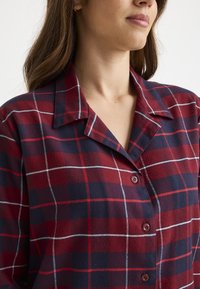 Camisa de cuadros en rojo y marinero con cuello, fabricada en un tejido suave y con líneas de rejilla blanca visibles en todo el diseño.