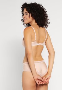 Conjunto de sutiã e calcinha rosa claro em tecido transparente com delicadas rendas. Alças ajustáveis e fecho de gancho no sutiã. Textura suave.