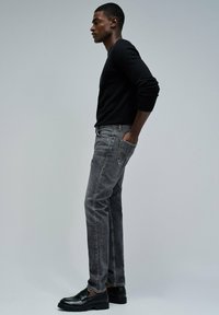 Camisa negra de manga larga combinada con jeans negros desgastados, con corte recto y bolsillo trasero. Mocasines negros completan el conjunto.